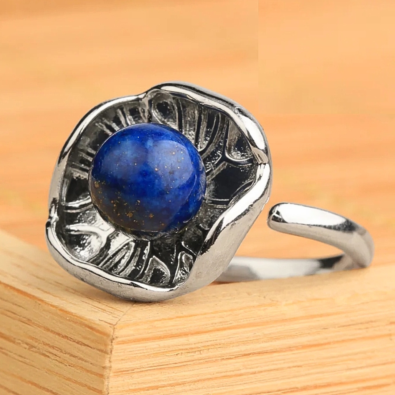 Bague en métal argenté au design lotus, centrée autour d’une pierre ronde bleue.