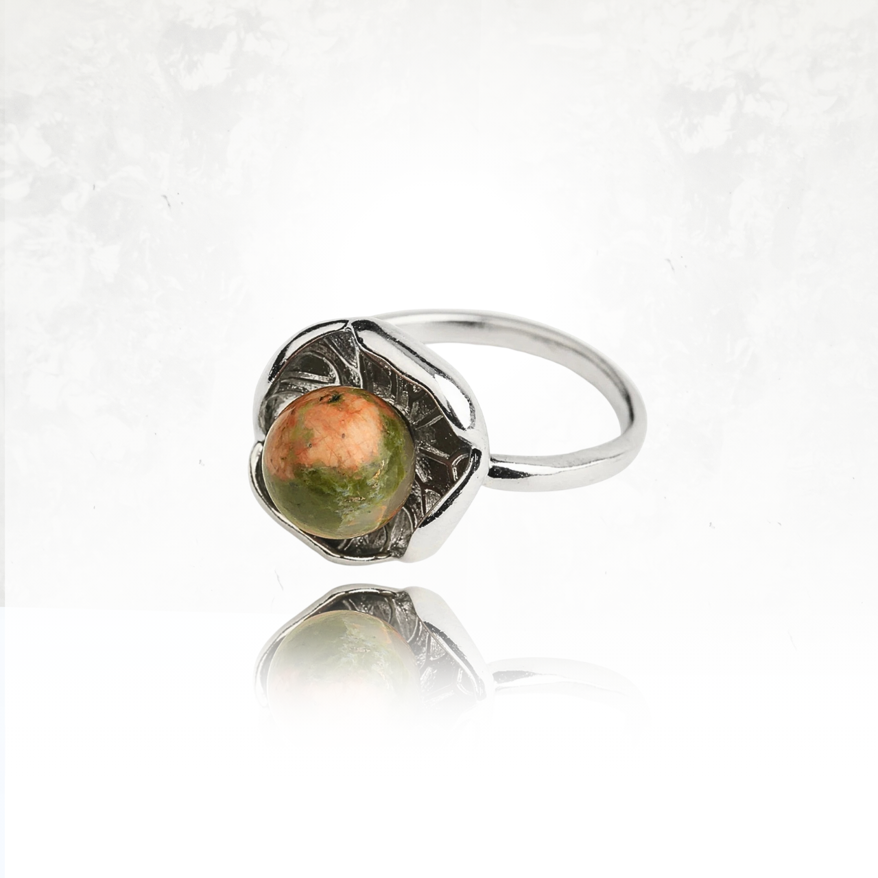 Bague argentée ornée d’une pierre ronde verte et marron évoquant un lotus épanoui.