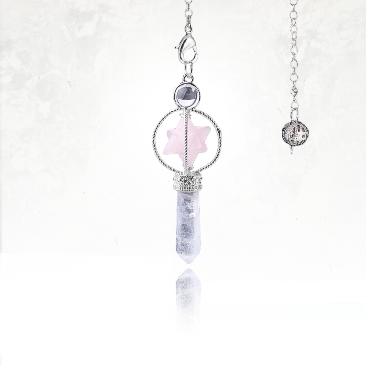 Pendule SINYA orné d’une Merkaba en pierre naturelle de quartz rose et d’une pointe hexagonale en quartz clair.